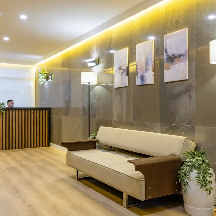 Sala de espera moderna con sof&aacute; beige, luz amarilla y cuadros en pared