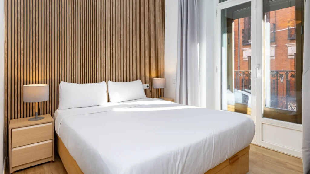 Dormitorio moderno con cama blanca, l&aacute;mparas y ventana con vista exterior