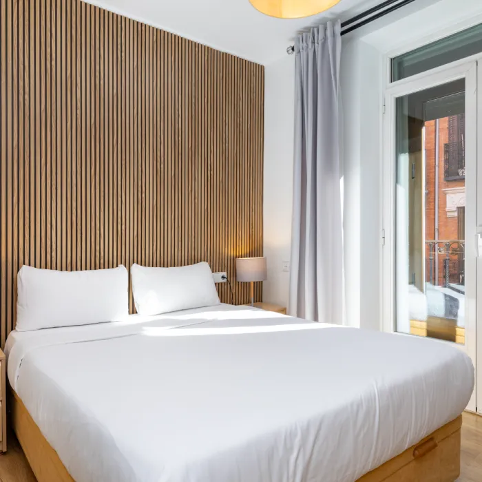 Dormitorio moderno con cama blanca, paredes de madera y ventana exterior