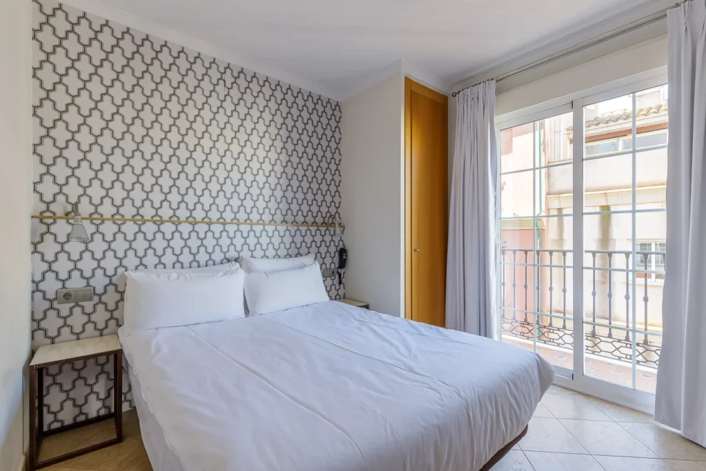Dormitorio moderno con cama blanca y pared de patr&oacute;n geom&eacute;trico, salida a balc&oacute;n