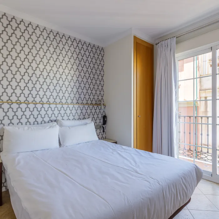 Dormitorio moderno con cama blanca, pared geom&eacute;trica y ventana con cortinas