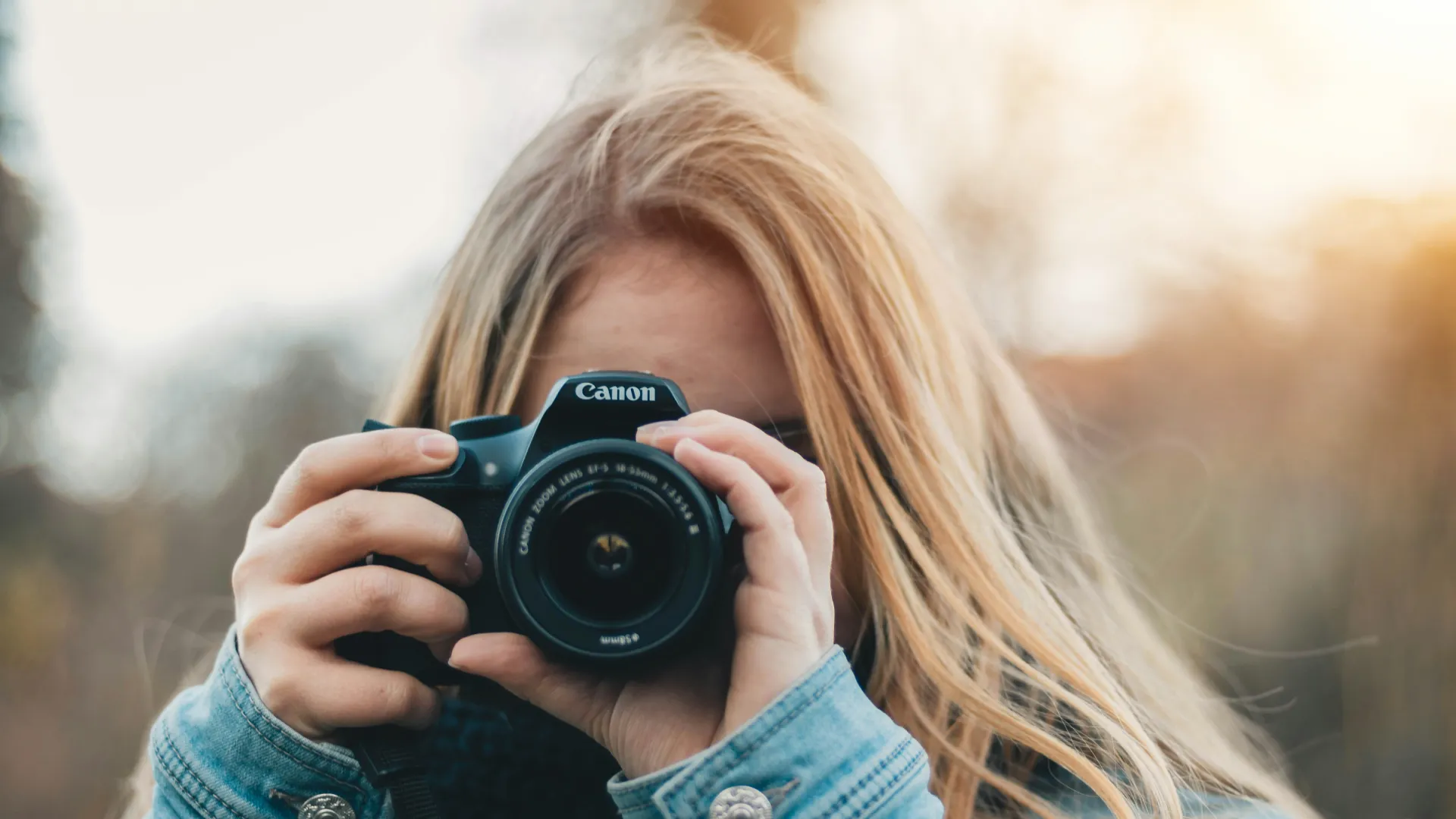 Mujer rubia fotografiando con una c&aacute;mara Canon, de frente y primer plano.
