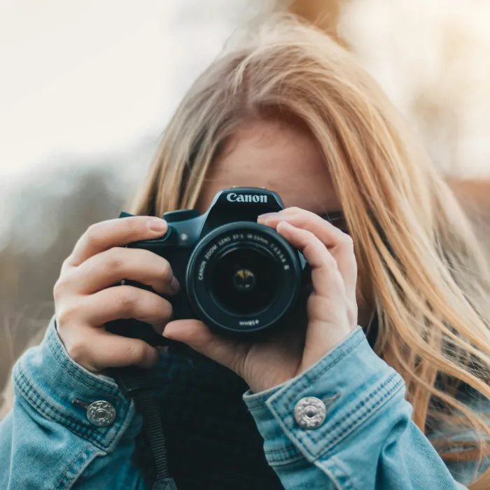 Mujer rubia toma una foto con c&aacute;mara Canon frente al rostro.