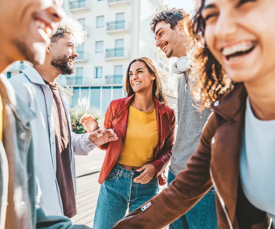 Amigos riendo y saludando en la calle, con edificios al fondo