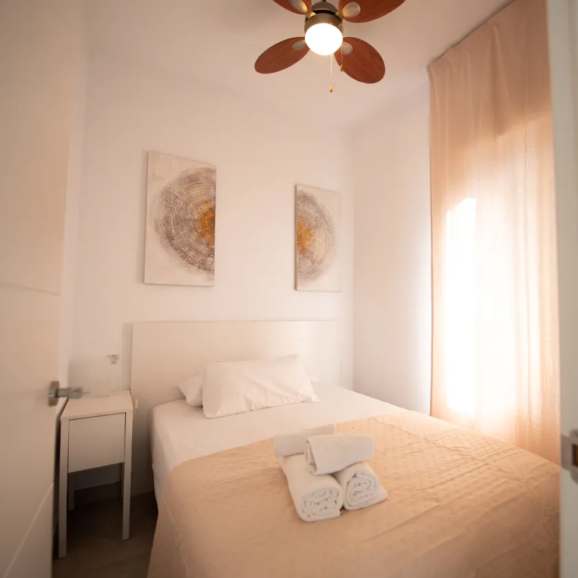 Dormitorio moderno con cama blanca, cojines y ventilador de techo.