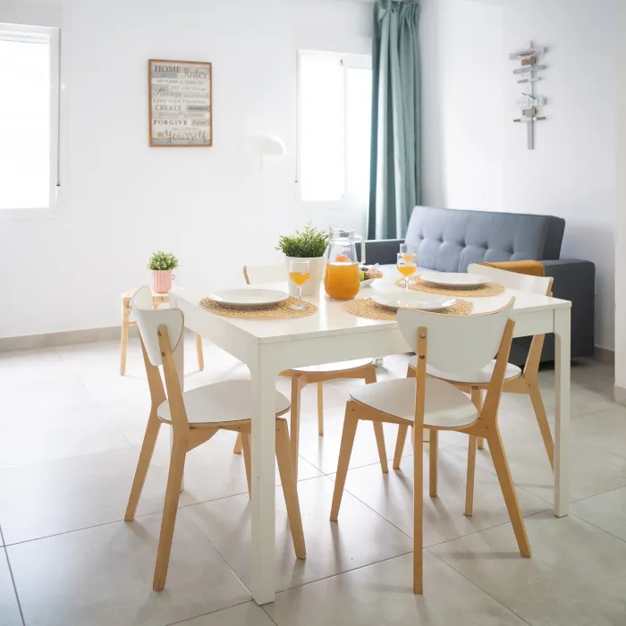 Comedor blanco con mesa, sillas de madera y bebida en vasos, sala luminosa