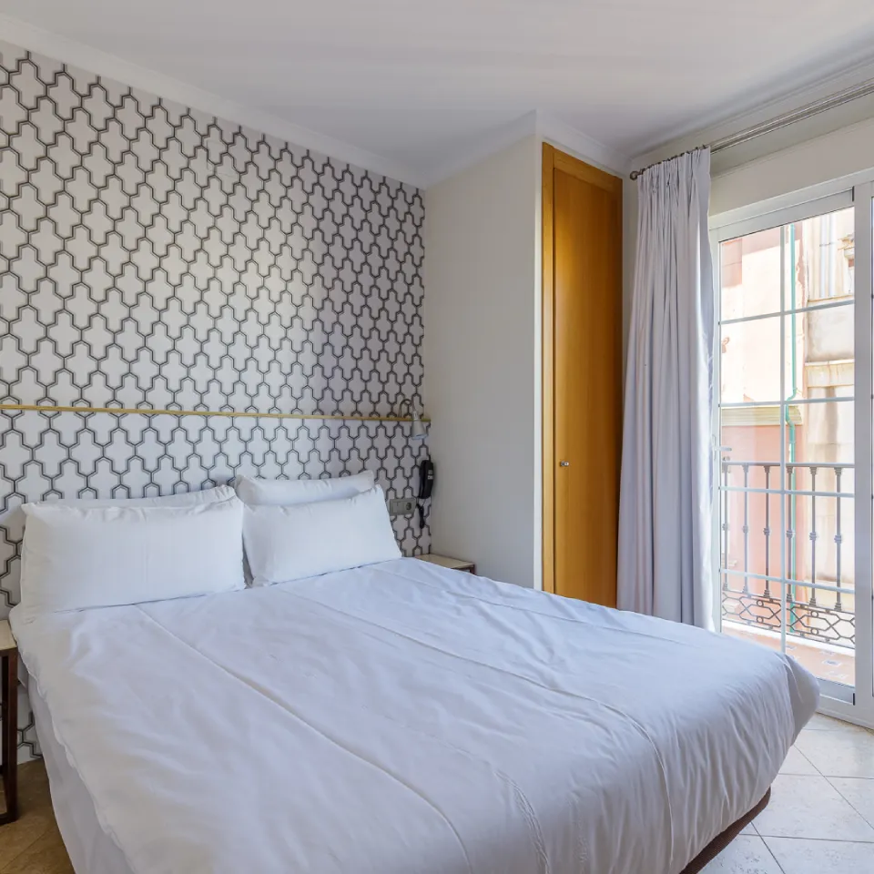 Dormitorio moderno con cama blanca y pared geom&eacute;trica, junto a una ventana