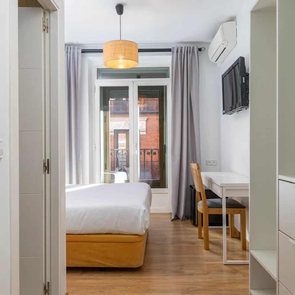 Dormitorio moderno con cama blanca, escritorio y ventana a la calle