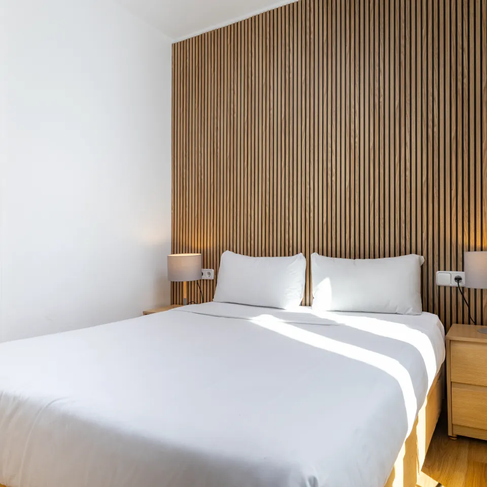Dormitorio moderno con cama blanca y pared de listones de madera con luz solar