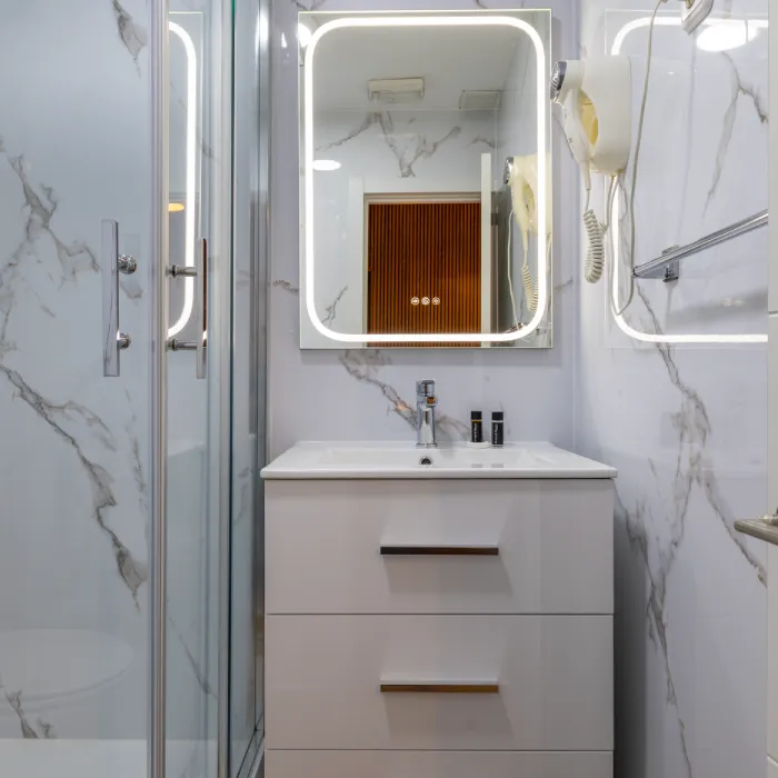 Ba&ntilde;o moderno blanco con lavabo, espejo y ducha de vidrio.
