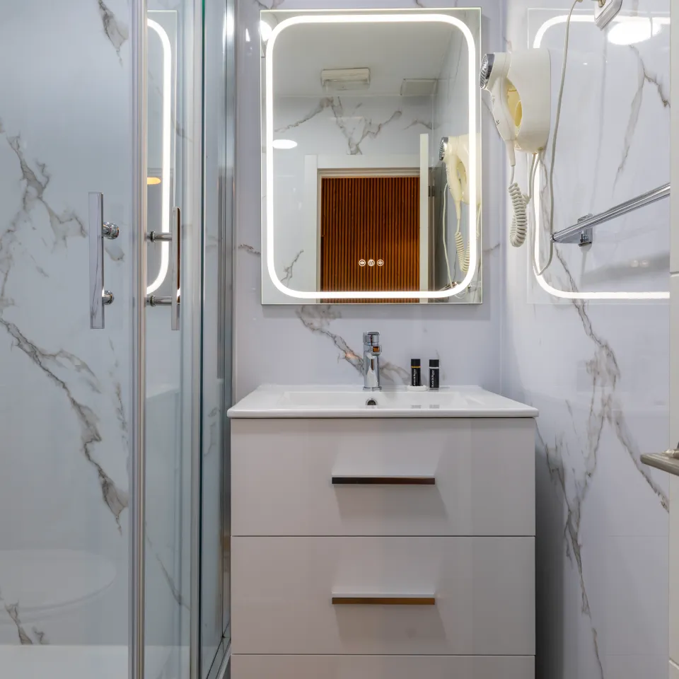 Ba&ntilde;o moderno blanco con lavabo, espejo iluminado y ducha de vidrio