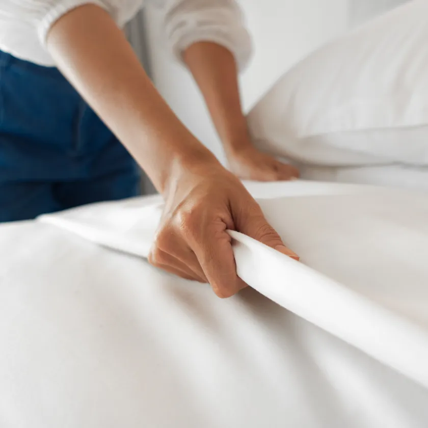 Manos arreglando s&aacute;banas blancas en una cama, hogar y limpieza