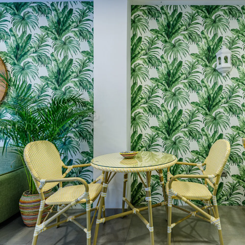 Mesa redonda y dos sillas de mimbre con pared de palmas verdes tropicales