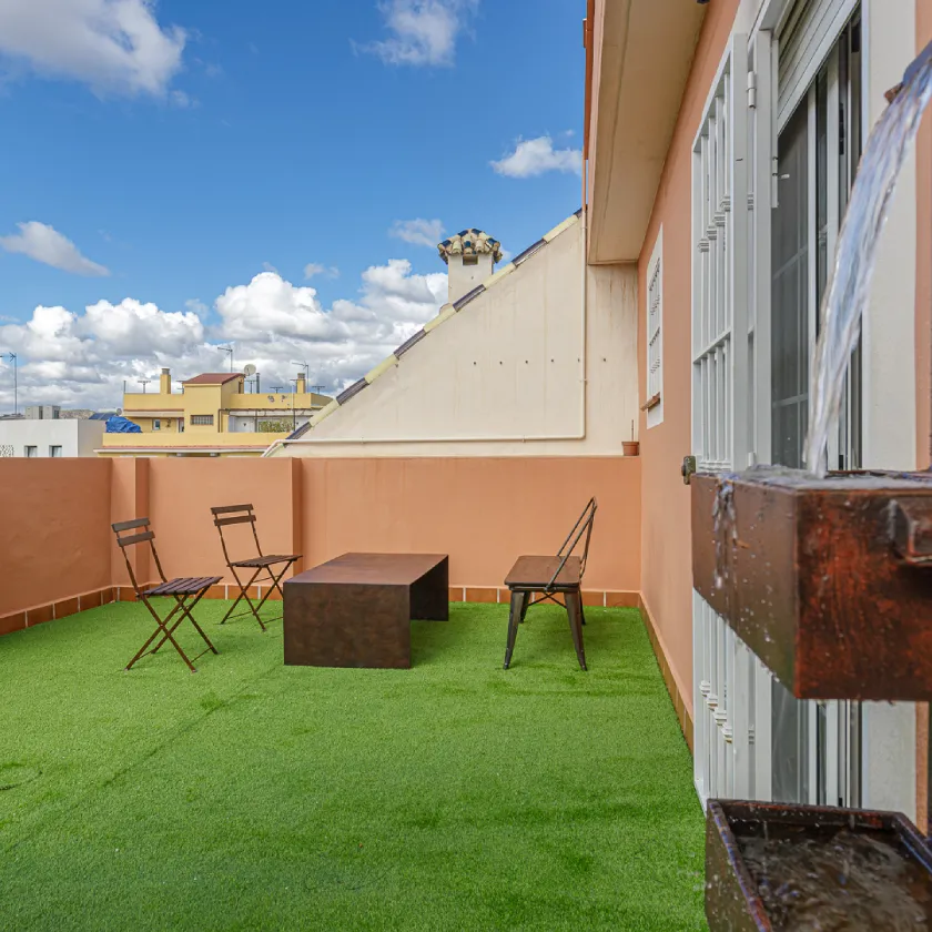 Patio con c&eacute;sped verde, muebles y paredes blancas bajo cielo parcialmente nublado
