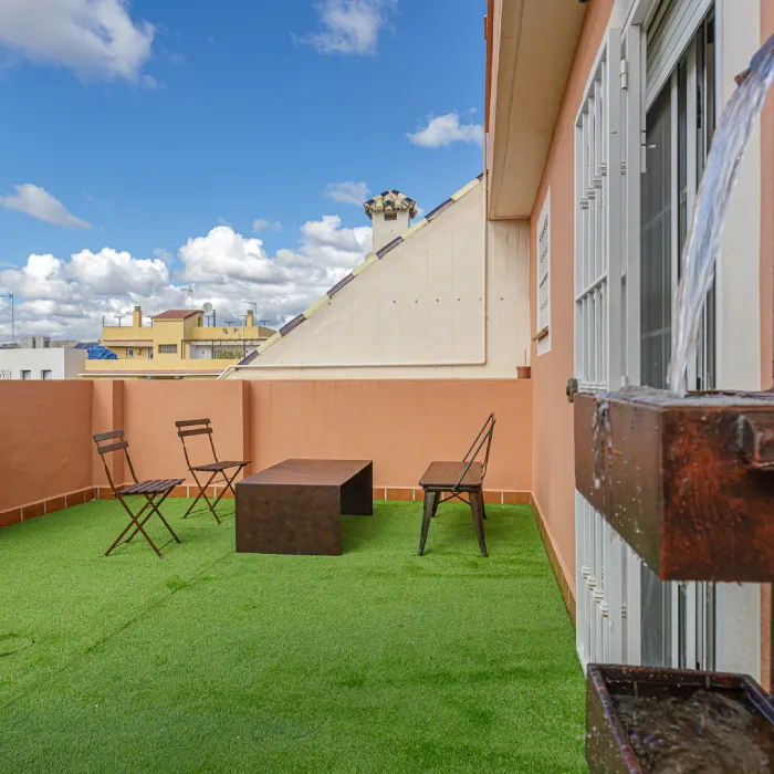 Terraza con c&eacute;sped verde y muebles junto a una pared, con cielo azul