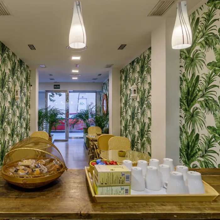 Interior de cafeter&iacute;a con mesas, sillas y paredes con estampado tropical.
