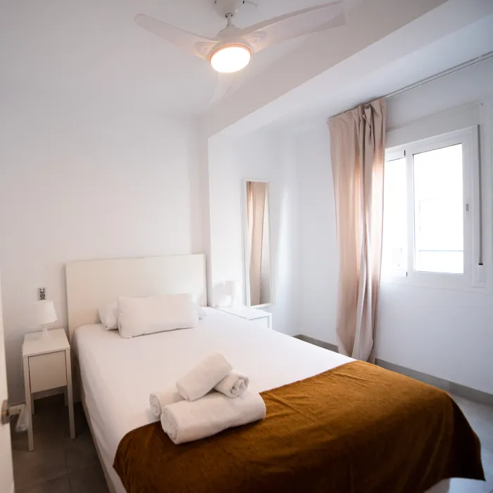 Dormitorio blanco con cama doble y cortinas beige frente a una ventana