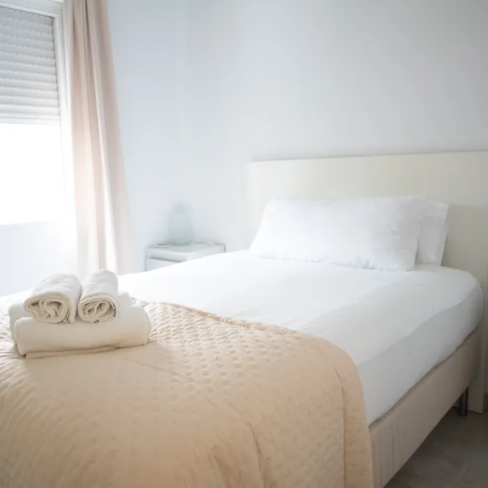 Dormitorio luminoso con cama doble y ropa de cama blanca, junto a ventana