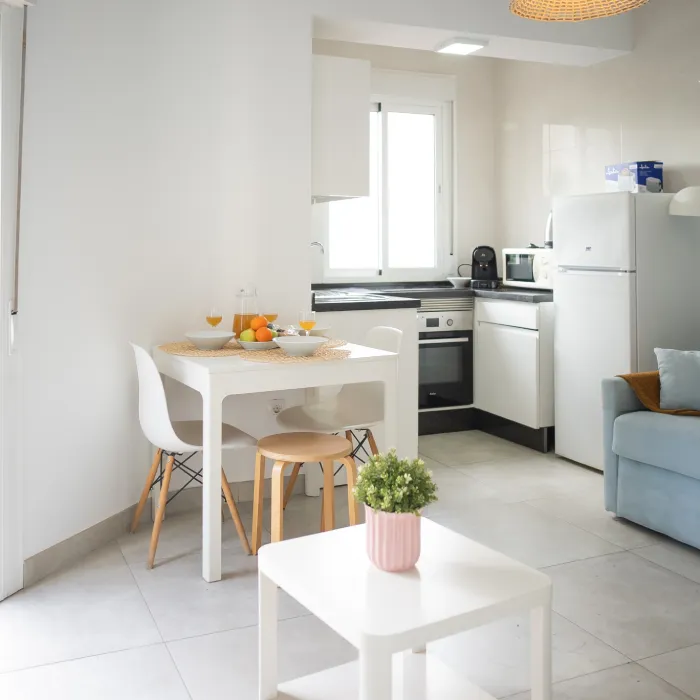 Cocina moderna blanca con mesa y sof&aacute;, luz natural y decoraci&oacute;n.