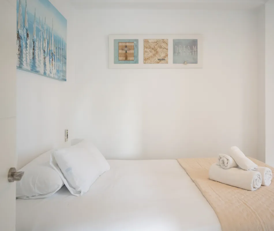 Habitaci&oacute;n blanca con cama doble y cuadros decorativos en la pared.