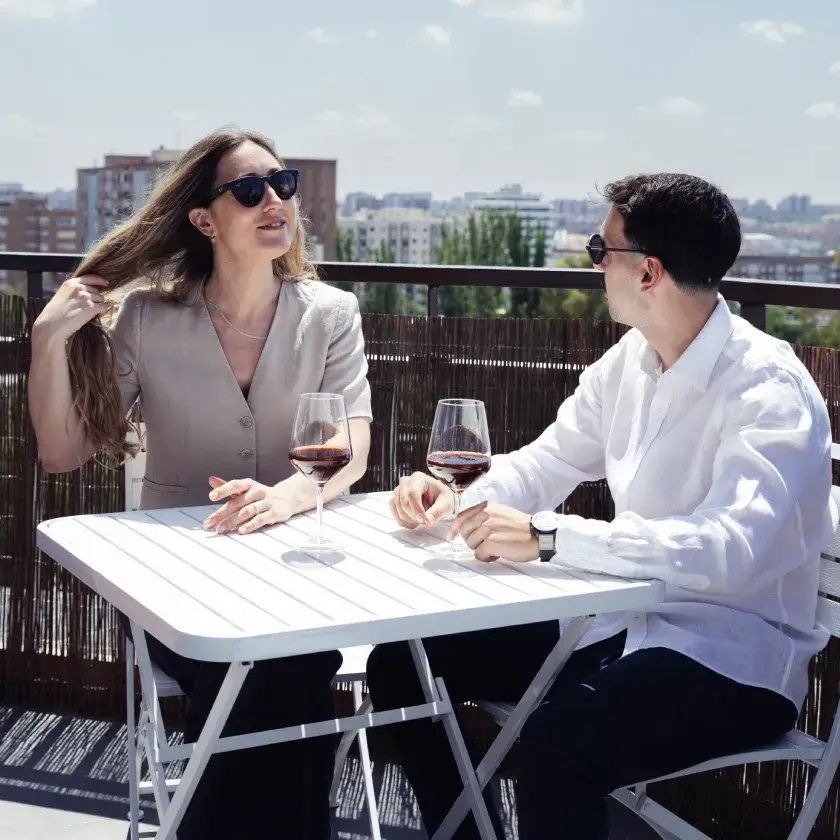 Dos personas brindan en una terraza con copas de vino al aire libre