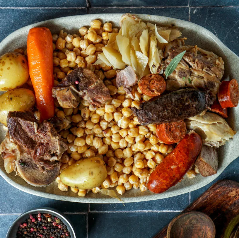 Plato de cocido con garbanzos, zanahoria, papa, carnes y repollo en caldo.