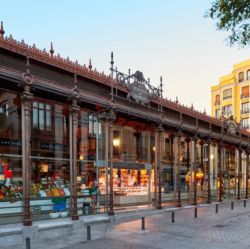 P&oacute;rtico de mercado de San Miguel, con columnas y tiendas al atardecer.