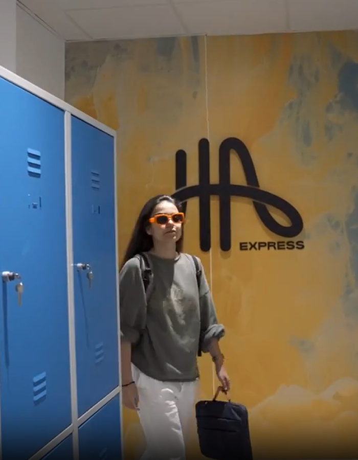 Persona con gafas y bolso junto a puerta azul, mural &ldquo;express&rdquo; al fondo.