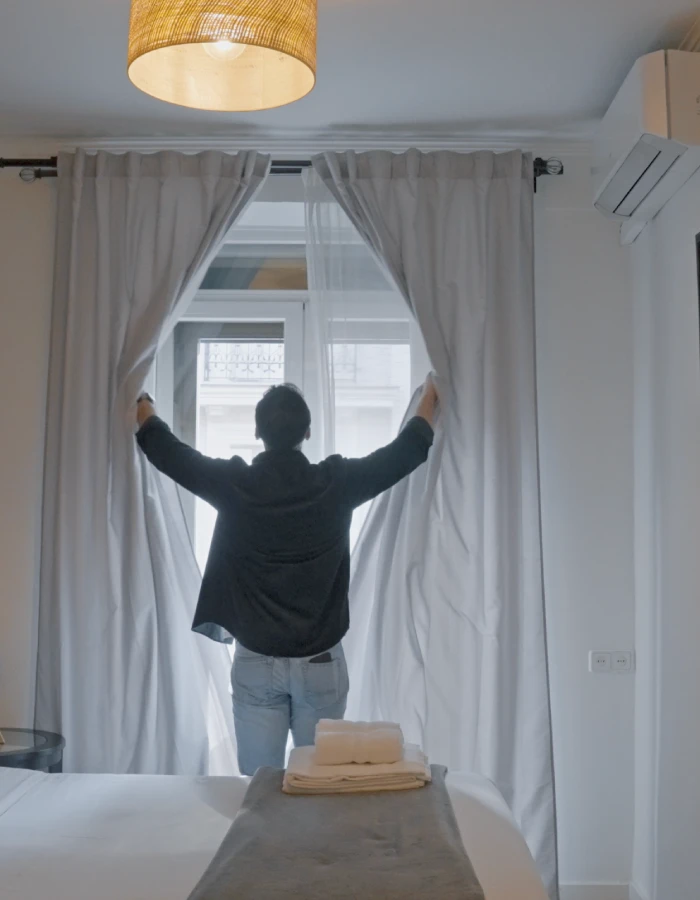 Persona ajustando las cortinas en una habitaci&oacute;n luminosa, de espaldas