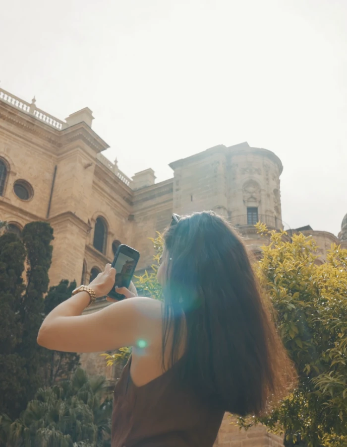 Mujer hace foto con m&oacute;vil frente a una iglesia y jardines al atardecer