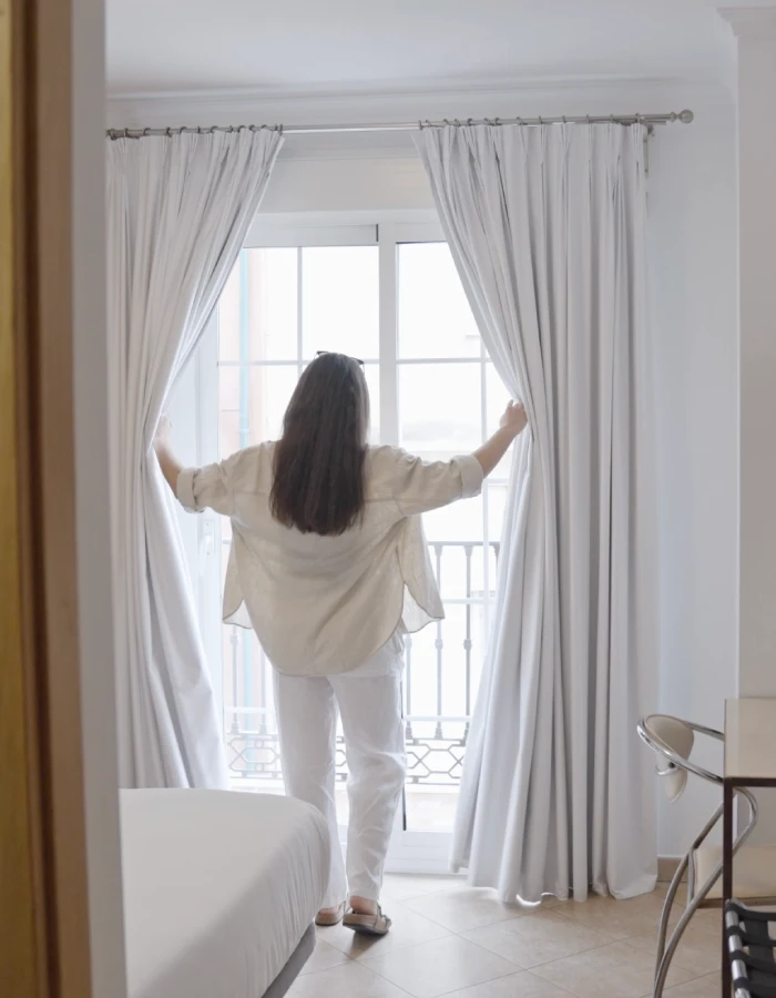 Mujer abriendo las cortinas blancas en una habitaci&oacute;n luminosa