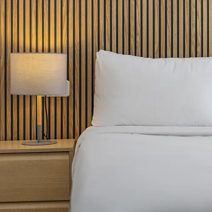 Dormitorio con cama y l&aacute;mpara de mesa junto a pared de madera.