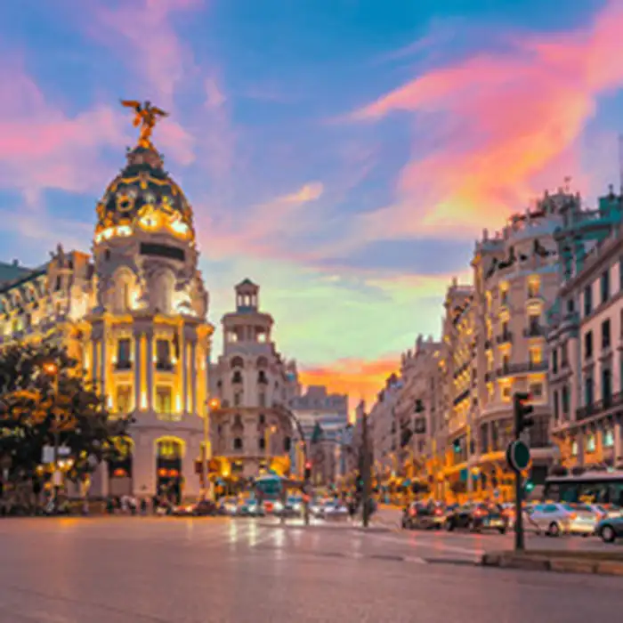 Calle de Par&iacute;s con edificios iluminados y cielo al atardecer, arco&iacute;ris y tr&aacute;fico.
