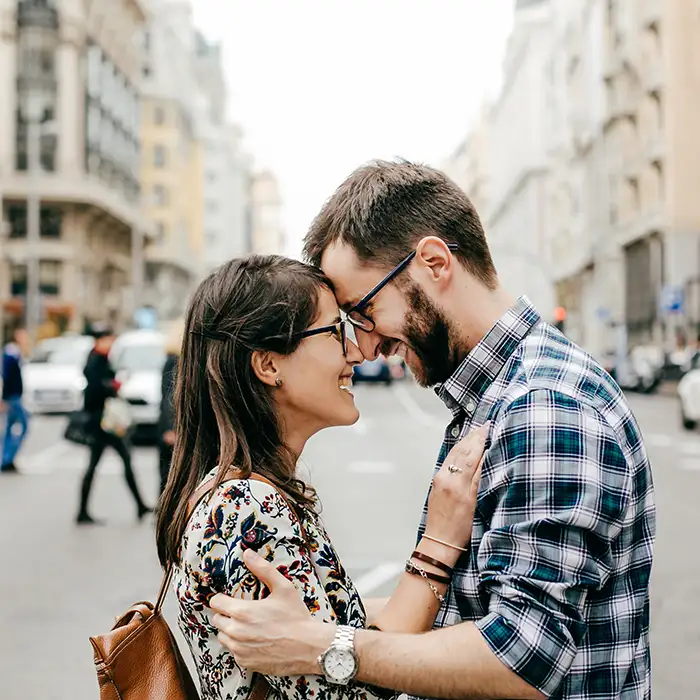 Pareja bes&aacute;ndose en la calle, con edificios al fondo