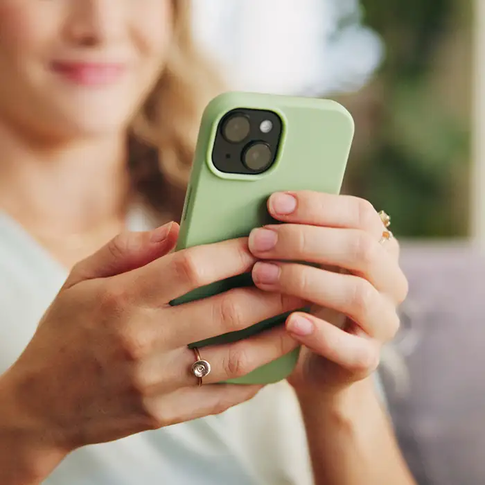 Mujer sujetando un tel&eacute;fono verde con ambas manos al aire libre