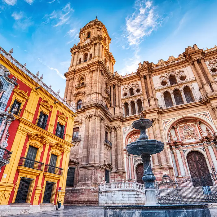 Catedral hist&oacute;rica con fuente y edificios de colores bajo cielo azul