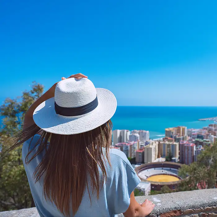 Mujer con sombrero blanco mirando el mar y la ciudad desde un mirador