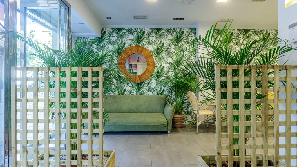 Sala interior con sof&aacute; verde, paredes con palmeras y paravientos de madera.