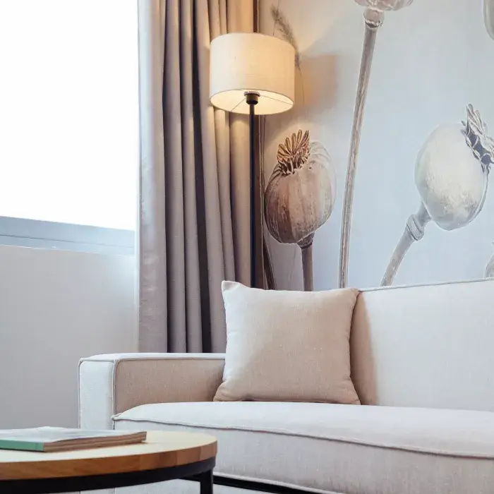 Sala con sof&aacute; claro, l&aacute;mparas y decoraci&oacute;n floral en pared blanca