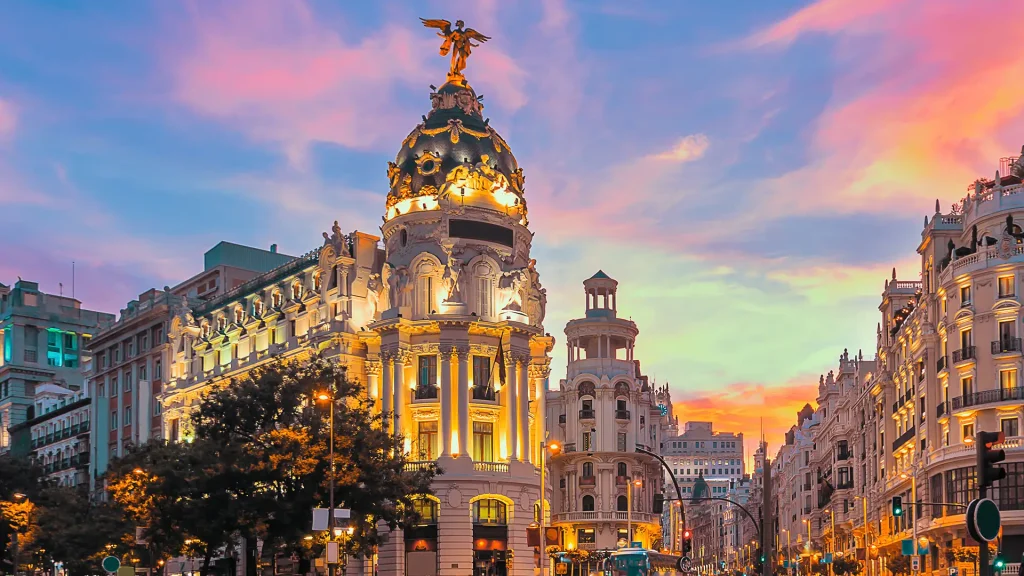 Edificio neobarroco con estatua de &aacute;ngel dorada al atardecer, en la Gran V&iacute;a