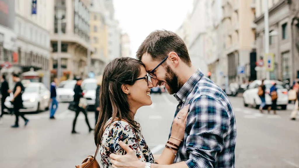 Pareja en la calle sonriendo, &eacute;l inclina la frente hacia ella