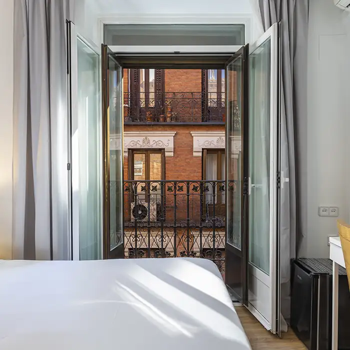 Dormitorio con cama y puerta abierta hacia un balc&oacute;n con barandilla met&aacute;lica