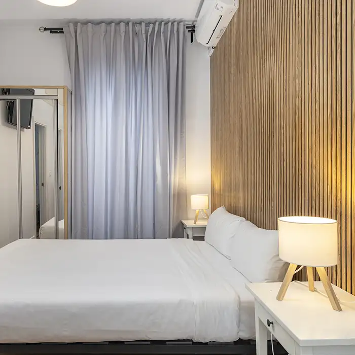 Habitaci&oacute;n moderna con cama blanca, l&aacute;mpara y cortinas grises.