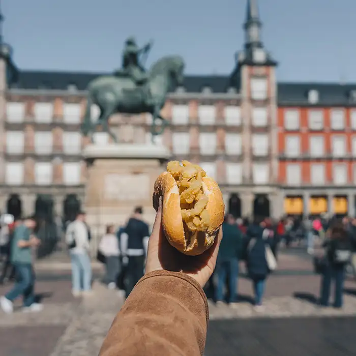 Mano con un bollito relleno de patata y multitud de fondo en la plaza
