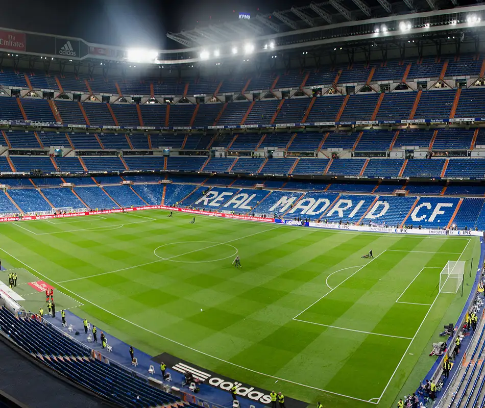 Estadio de f&uacute;tbol con el campo iluminado y gradas vac&iacute;as, partido en curso