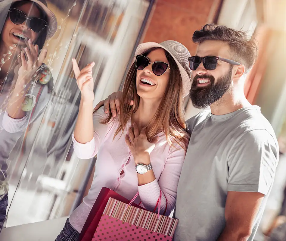Pareja joven con gafas de sol y bolsas de compras, sonriendo en la calle