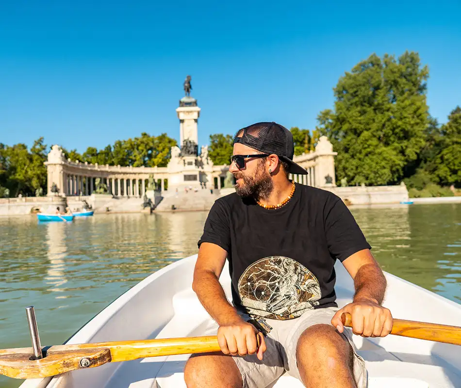 Hombre con gorra negra en lancha frente al lago y una torre hist&oacute;rica.