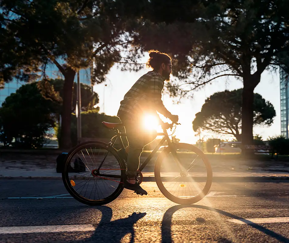 Hombre en bicicleta al atardecer, con rayos de sol entre &aacute;rboles