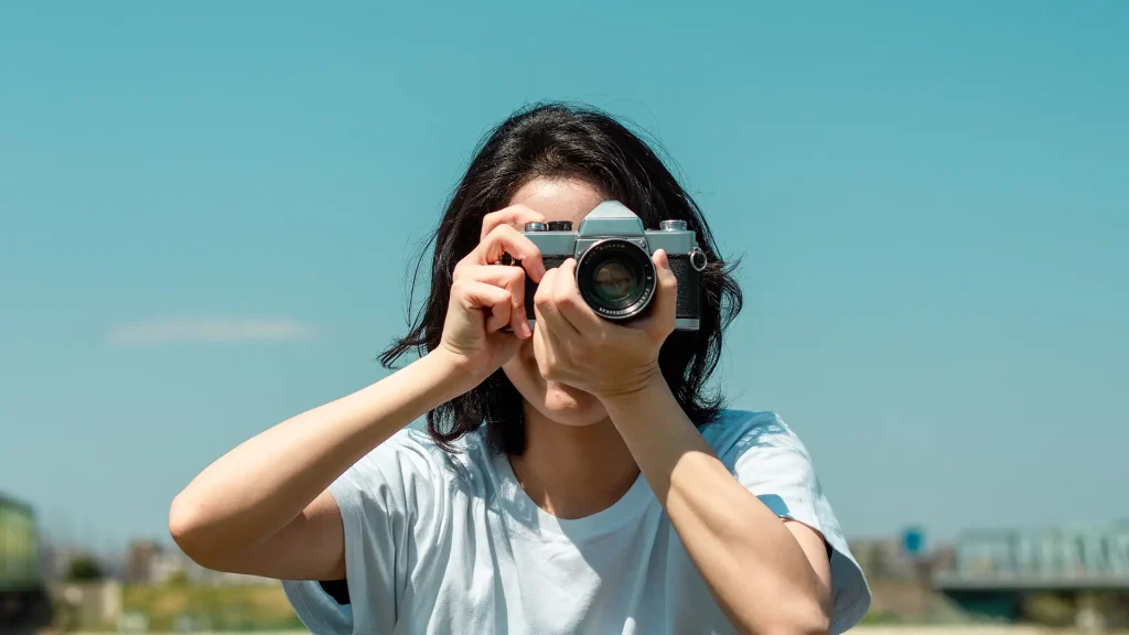 Mujer con c&aacute;mara fotogr&aacute;fica en exterior, apuntando al lente