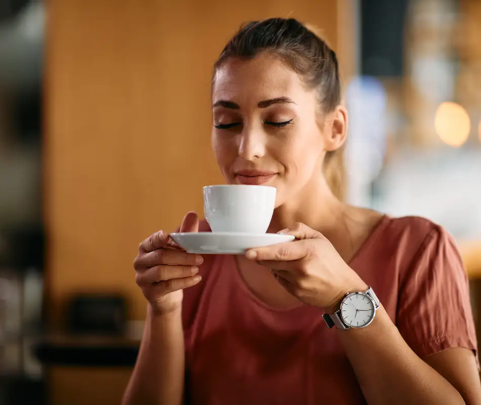 Mujer sonriente sosteniendo una taza de caf&eacute; en un entorno c&aacute;lido